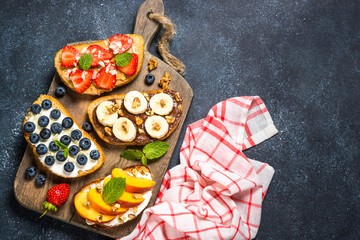 Sweet toast assortment on black background. Chocolate banana, cream cheese and peach, peanut butter and strawberry, cream cheese and blueberry toasts.