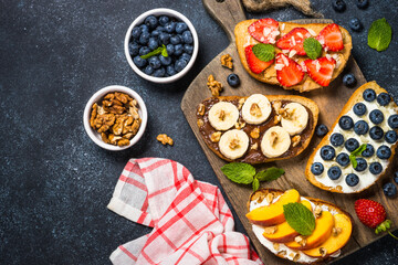 Sweet toast assortment on black background. Chocolate banana, cream cheese and peach, peanut butter and strawberry, cream cheese and blueberry toasts.