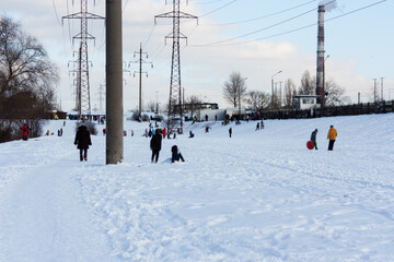 Children and their parents sledding from a snow slide in a city park with a frozen lake in Kiev, Ukraine