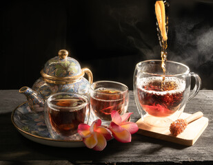 Tea cup of freshly brewed fruit and herbal tea with Plumeria flower and traditional kettle on dark...
