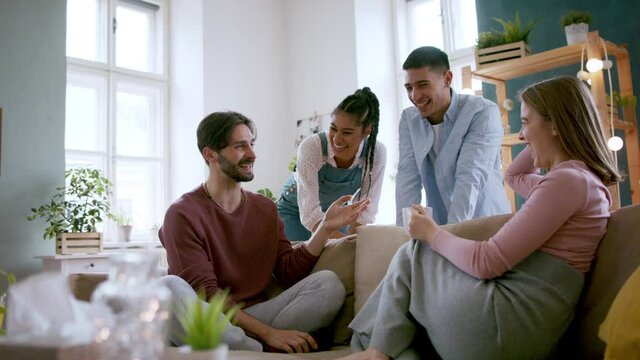Young friends sitting on sofa indoors having a funny conversation, house sharing concept.