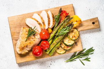 Chicken breast grilled with vegetables on a wooden serving board. Barbecue dish. Top view on white...
