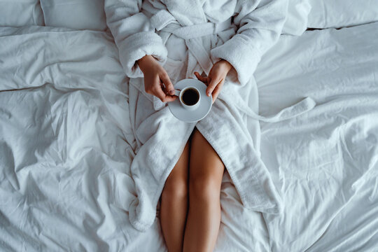 Lazy woman wearing bathrobe lying on bed and enjoying aromatic coffee cup during relaxing at cozy comfort bedroom at hotel room. Easy lifestyle. Beginning of new day