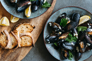 Cooked shell mussels in cheese sauce with lemon in ceramic plates.