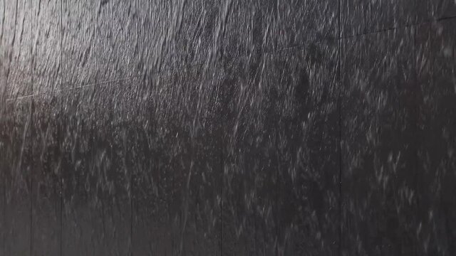 Black stone wall with water flowing down. Modern swimming pool or fountain in a shopping center