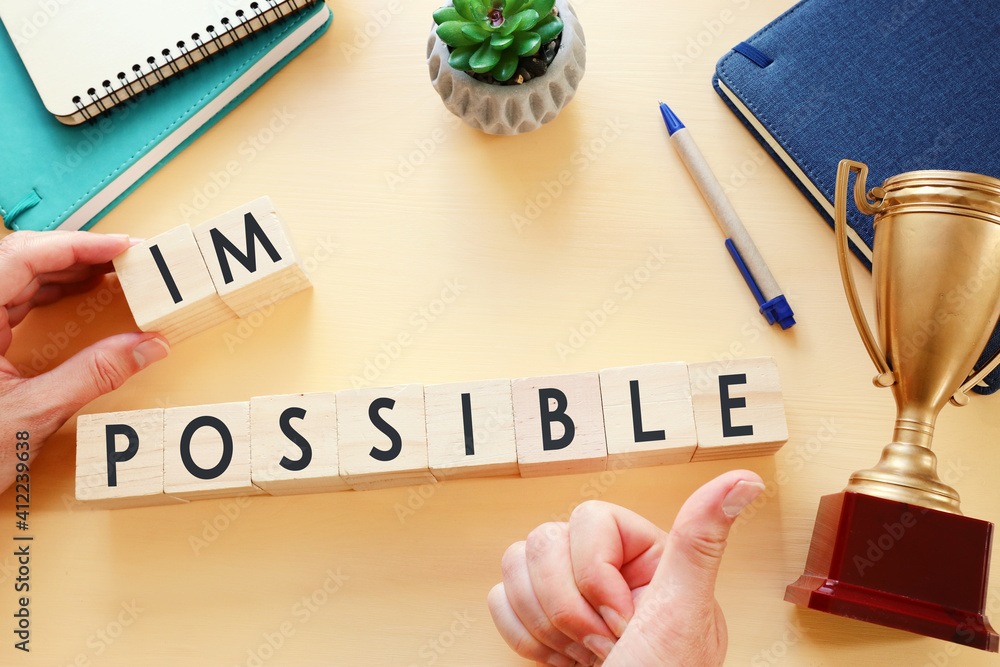 Poster man hand holding wooden cubes with the text impossible, removing the word im so it written possible.
