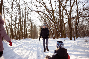 Fototapeta na wymiar The boy is taking his younger brother on a sleigh along a snowy road in the forest. Children's rest in winter.