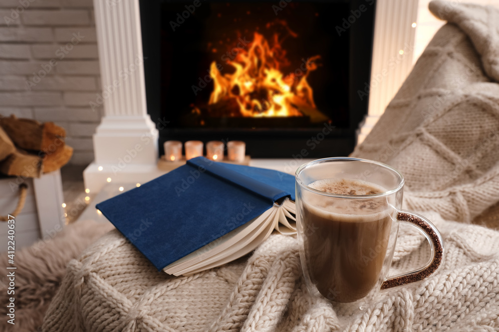 Poster Cup of coffee and book on plaid near fireplace indoors. Cozy atmosphere