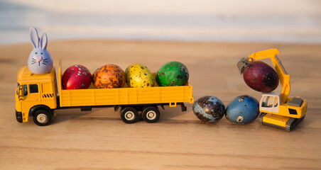 orange models of toy excavator and dump trucks with Easter quail eggs painted with rainbow colors. Easter holiday concept for business building companwith Easter quail eggs painted with rainbow colors © Anna