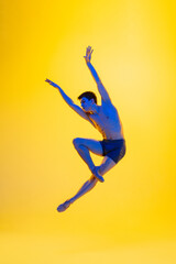 Fototapeta na wymiar Artwork. Young and graceful ballet dancer on yellow studio background in neon light. Art, motion, action, flexibility, inspiration concept. Flexible caucasian ballet dancer, moves in glow.