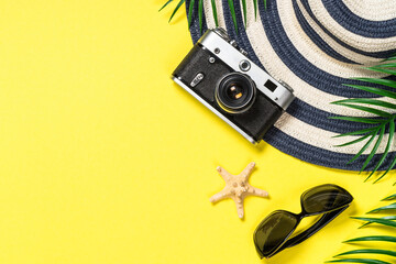 Summer travel flat lay background. Old film camera, hat, sunglasses, shell and palm leaves on yellow background.