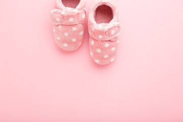 Beautiful soft warm baby girl slippers on light pink table background. Pastel color. Closeup. Comfortable home shoes. Empty place for text. Top down view.