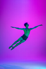 Flying. Young and graceful ballet dancer on purple studio background in neon light. Art, motion, action, flexibility, inspiration concept. Flexible caucasian ballet dancer, moves in glow.