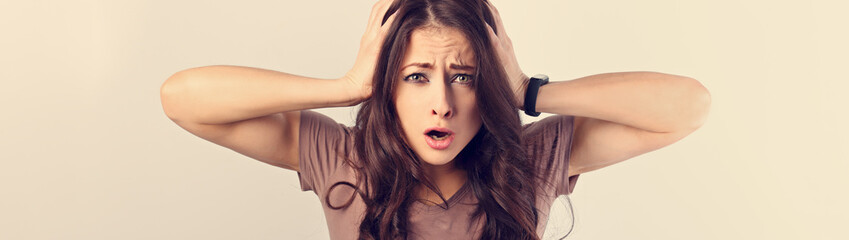 Fototapeta premium Angry young surprising business woman holding the head the hands with big eyes. Fun humor casual portrait on toned brown background with empty space