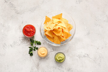 Bowl with tasty nachos and sauces on light background