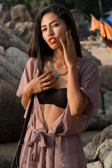 Stunning asian woman in summer outfit posing on the brach. Rocks on backgroud.