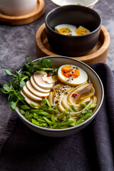 Bowl of asian ramen soup with noodles, spring onion, sliced egg and mushrooms on black table. Japanese dish in black. 
