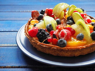 Cake with berries and exotic fruits - raspberry, blueberry, red currant, kiwi, apple, strawberry, orange, mango