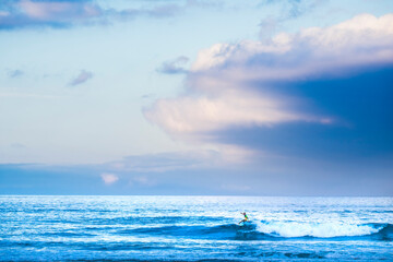 Surfer tourist athlete do surf water sport activity alone in the blue ocean waves - colorful sky in background and concept of healthy brave people in extreme lifestyle leisure