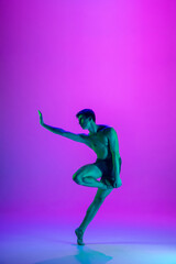 Performing. Young and graceful ballet dancer on purple studio background in neon light. Art, motion, action, flexibility, inspiration concept. Flexible caucasian ballet dancer, moves in glow.