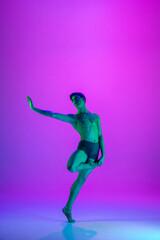 Obraz na płótnie Canvas Performing. Young and graceful ballet dancer on purple studio background in neon light. Art, motion, action, flexibility, inspiration concept. Flexible caucasian ballet dancer, moves in glow.