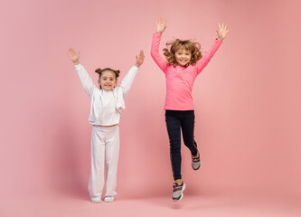 Flying on. Happy kids, girls isolated on coral pink studio background. Look happy, cheerful. Copyspace for ad. Childhood, education, emotions, facial expression concept. Jumping high, having fun