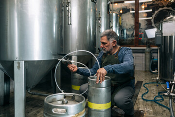 brewer working in his craft beer brewery. top up barrels of beer