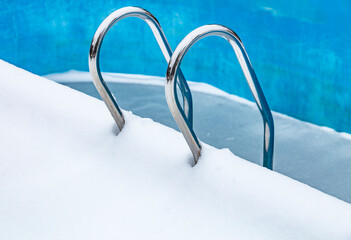 Empty swimming pool outdoor in the winter. Ladder, hand-rails and pool bottom covered by snow. Frozen swimming pool.