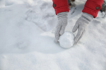 Young woman rolling snowball outdoors on winter day, closeup. Space for text