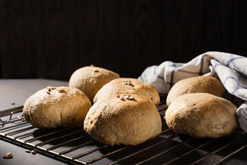 Homemade wholemeal rye wheat buns with seeds on wooden table, dark rustic background.