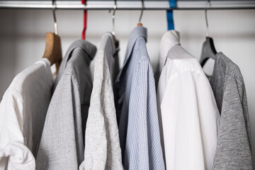 Row of cotton shirts and t-shirts hanging in the wardrobe. Simple casual unisex style, similar dressing options, textile, fashion