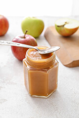 Jar of sweet apple jam and spoon on light background