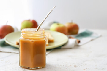 Jar of sweet apple jam and spoon on light background