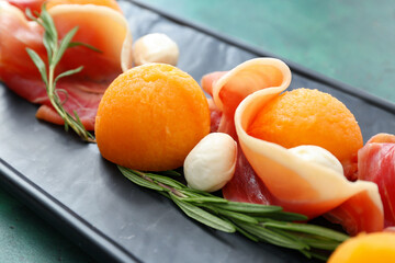 Board with delicious melon, mozzarella and prosciutto on color background, closeup
