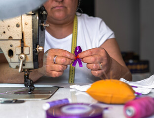Working woman, woman sewing purple ribbon on face masks. women's Day. Gender violence