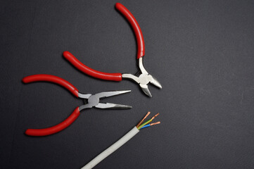 Pasatizh and wire cutters are in place with a stripped three-core wire. dark background.