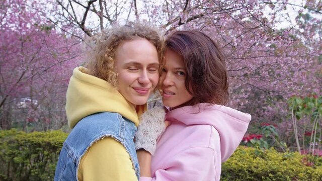 lesbian couple hugging in a sakura garden. Two women share love and support while holding hands. Gay Family. LGBT concept of friendship. cinematic chot bmpcc 6k