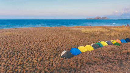 Camping with colorful tents in Kenawa Island, Sumbawa, Indonesia. Beautiful yellow grass with blue sea and sky