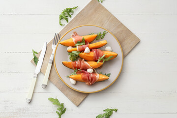 Plate with delicious melon, mozzarella and prosciutto on light background