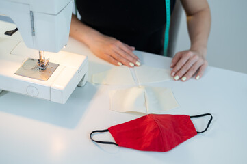 Close-up. A faceless woman sews masks on an electric sewing machine