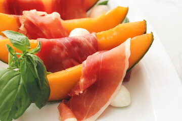 Plate with delicious melon, mozzarella and prosciutto on light background, closeup