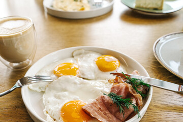 Bright breakfast on brown wooden background, front view. Tasty fried eggs and cup of coffee.