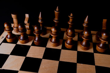 Black wooden pieces on a chessboard. A chessboard set up during a game on a black background