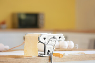 Pasta maker with dough on table in kitchen