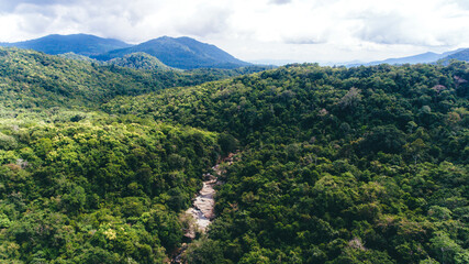 Drone shot aerial view top angle rain forest in Sumbawa, Indonesia. Lush green thick dense woods river bridge mountains bright sunny day beautiful weather valleys terrain nature streams