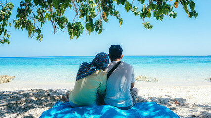 Happy honeymoon vacation at Paradise. Couple relax on the white sand of beach. Happy sea lifestyle. Young family, man and hijab woman rest on the beach of ocean. Couple in love travel to island.