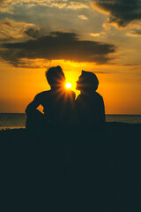 Slihouette young couple sitting on the beach near the sea and see each other with sunset as background.
