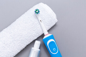 Electric toothbrush, toothpaste, and white towel on a gray background. Flat lay. The concept of electronic devices for personal hygiene