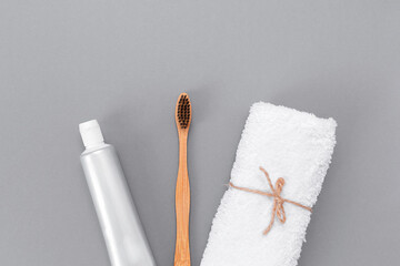 A roll of white towel, toothpaste, and a bamboo toothbrush. Flat lay. Gray background. The concept of eco-friendly personal care products