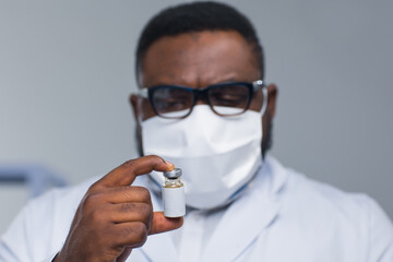 Professional African-American scientist is working on a vaccine in a modern scientific research laboratory. Doctor is looking on a vaccine tube. Future technology and science.